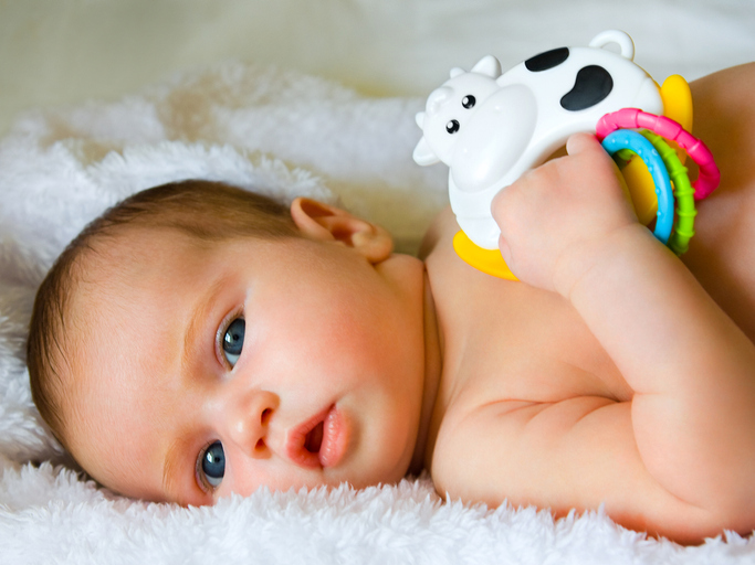 Baby on fluffy white towel holding toy of cow and colorful rings